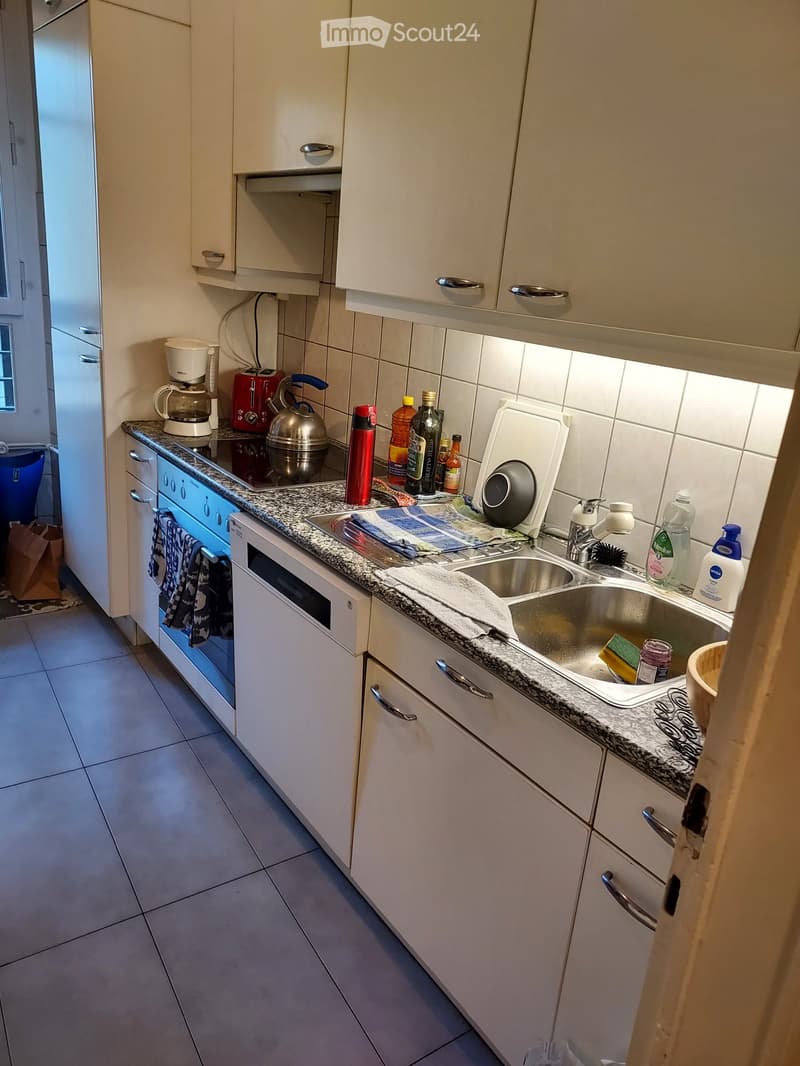 Modern kitchen with white cabinets, granite countertop, stainless steel sink, coffee maker, toaster, kettle, and various bottles on the counter.