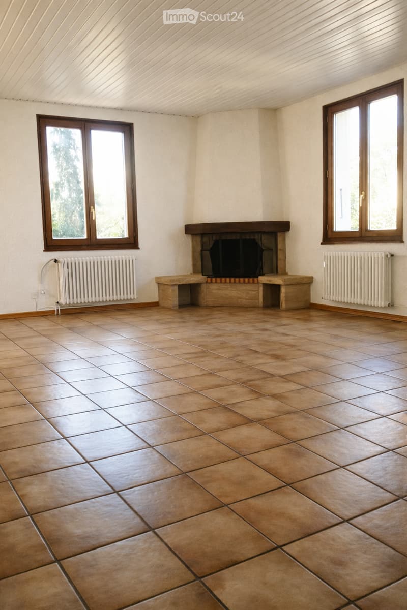 Empty room with tiled floor, fireplace, radiators, and large windows with wooden frames.