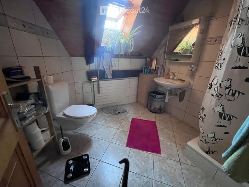 Bathroom with a toilet, sink, bathtub, mirror, and a shower curtain. Includes a pink bath mat, a small plant on the windowsill, and a scale on the floor.