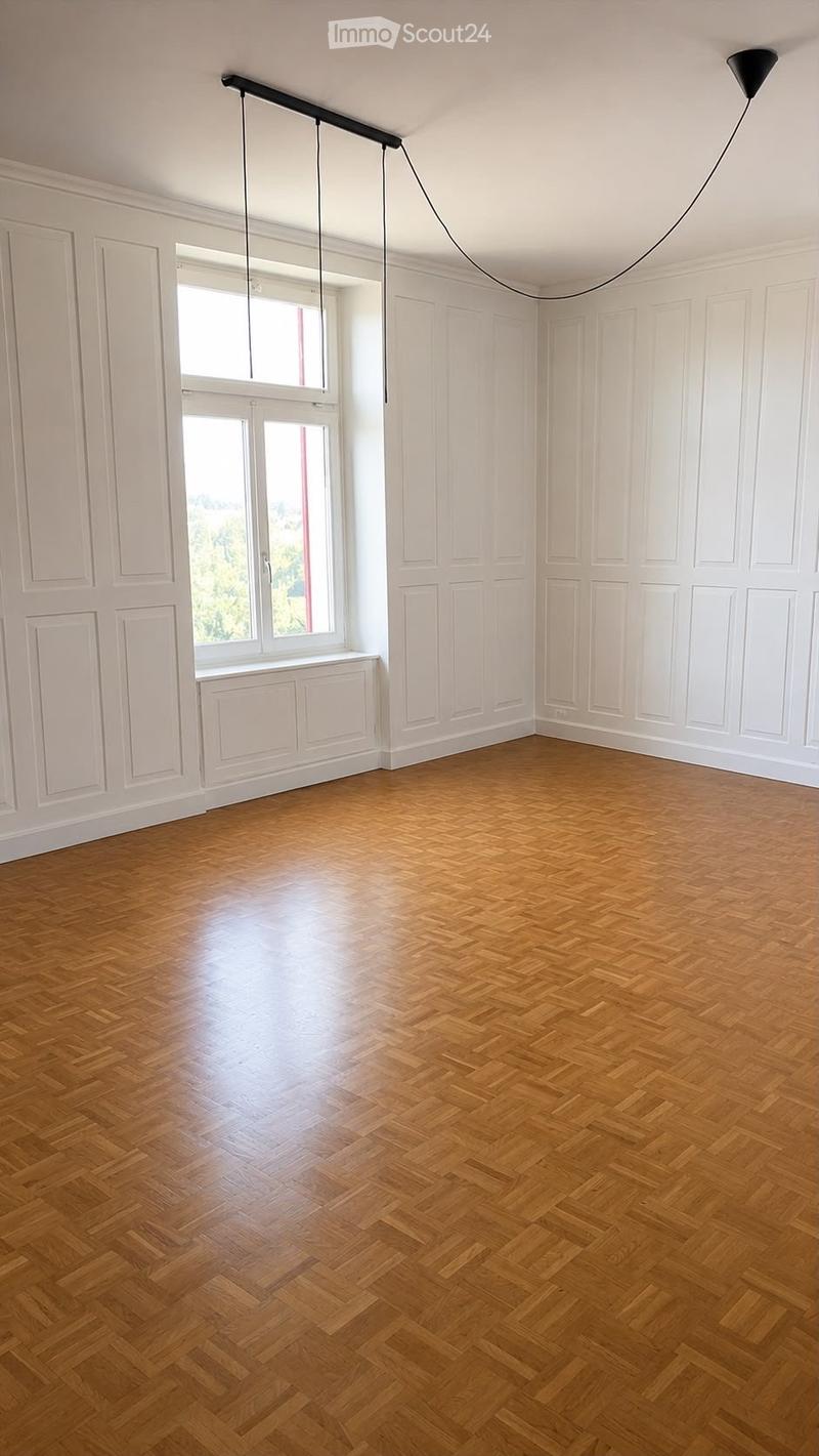 Empty room with wooden herringbone flooring, white paneled walls, large windows, and a modern pendant light fixture.