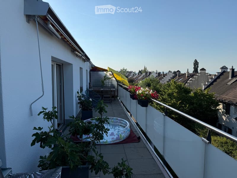 Balcony with tiled floor, metal railing, small inflatable pool, potted plants, and outdoor furniture including chairs and a table.