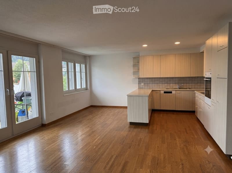 Bright, modern kitchen with light wood cabinets, a central island, and a polished hardwood floor. The space features a sink, faucet, and dishwasher, with large windows and a sliding glass door leading to an outdoor area.