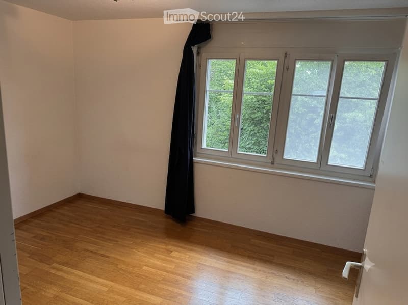 Empty room with wooden flooring, large window with black curtain, and white walls.