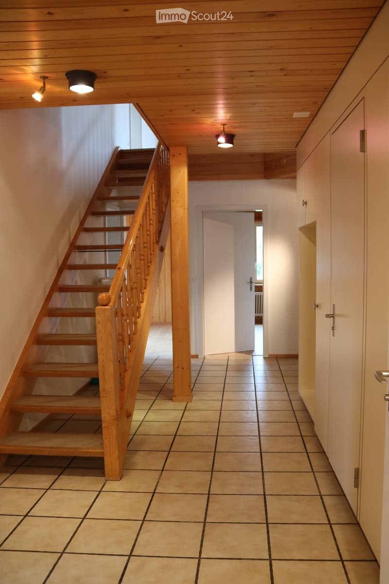Hallway with tiled floor, wooden staircase with railing, and built-in cabinets on one side.