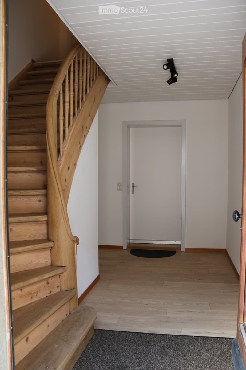 Wooden staircase with balustrade, light-colored walls, wooden floor, and a closed door leading to another room.