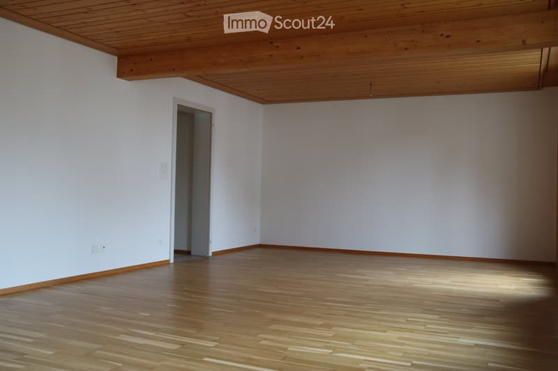 Empty room with light wooden flooring, white walls, and a wooden slanted ceiling. There is a doorway leading to another space.