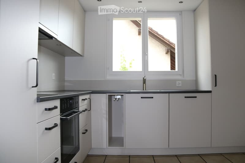 Modern kitchen with white cabinets, black countertops, and a built-in oven. Features a window above the sink and sleek, contemporary design.