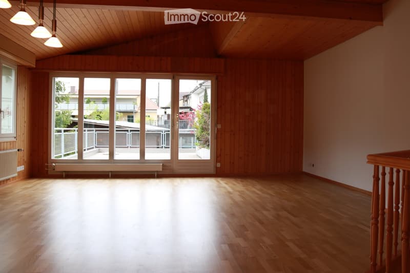 Empty room with wooden walls, wooden floor, large windows, and a balcony area visible through the glass doors.