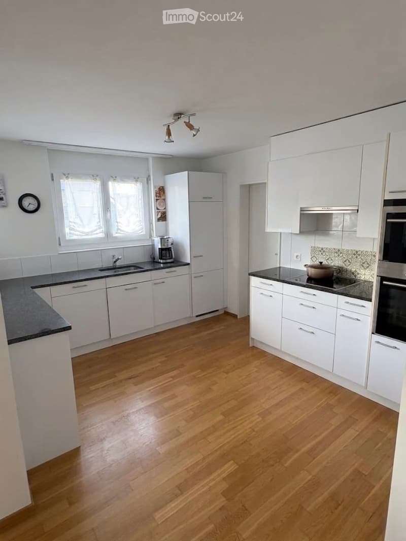 Modern kitchen with white cabinets, wooden flooring, stainless steel appliances, and a black countertop.