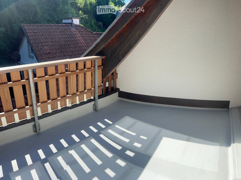 Roof terrace with wooden railing, white concrete floor, and a view of neighboring houses and greenery.