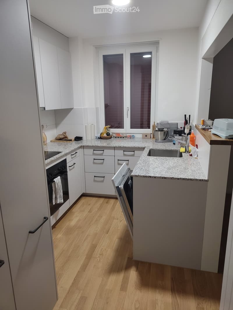 Modern kitchen with white cabinets, granite countertops, wooden flooring, and various appliances including an oven, dishwasher, and blender.
