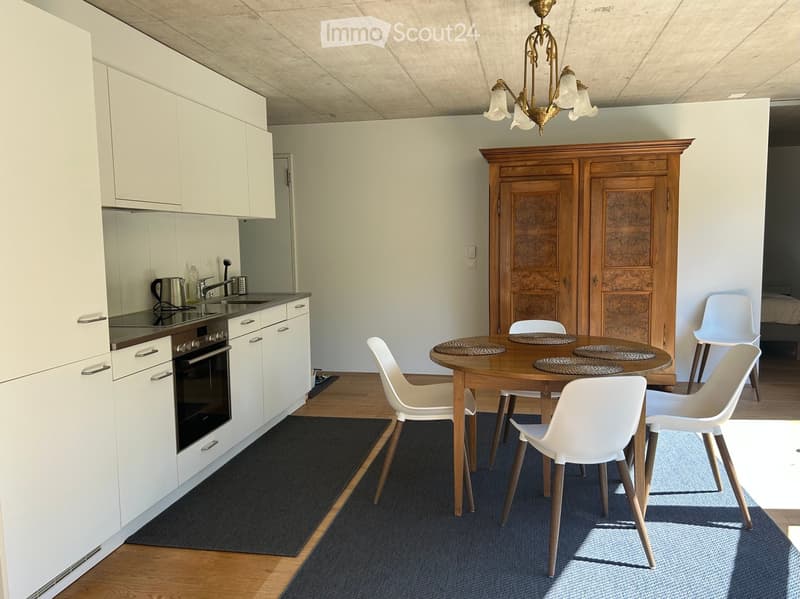 A modern kitchen and dining area with white cabinets, a wooden dining table, white chairs, and a chandelier.