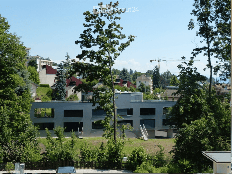Modern two-story building with large windows and a flat roof, surrounded by trees and greenery.