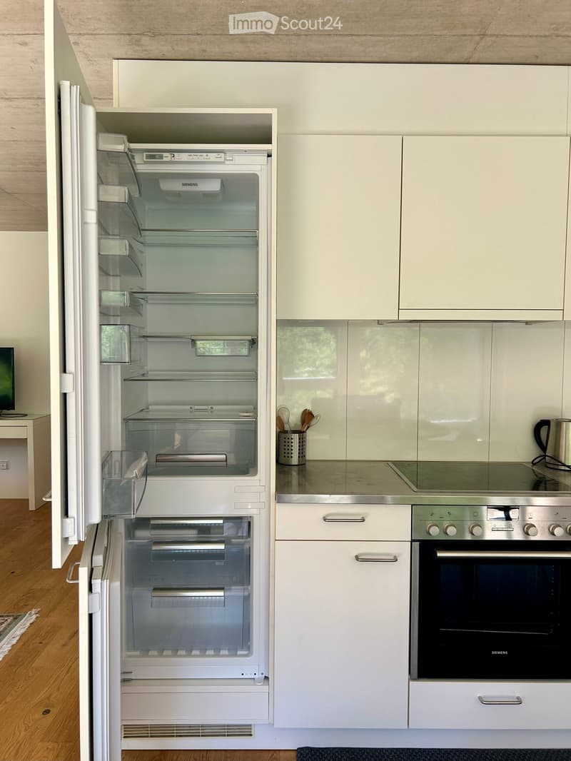 Modern kitchen with white cabinets, stainless steel appliances, and a sleek design. Features a refrigerator, oven, stove, and various kitchen utensils on the counter.