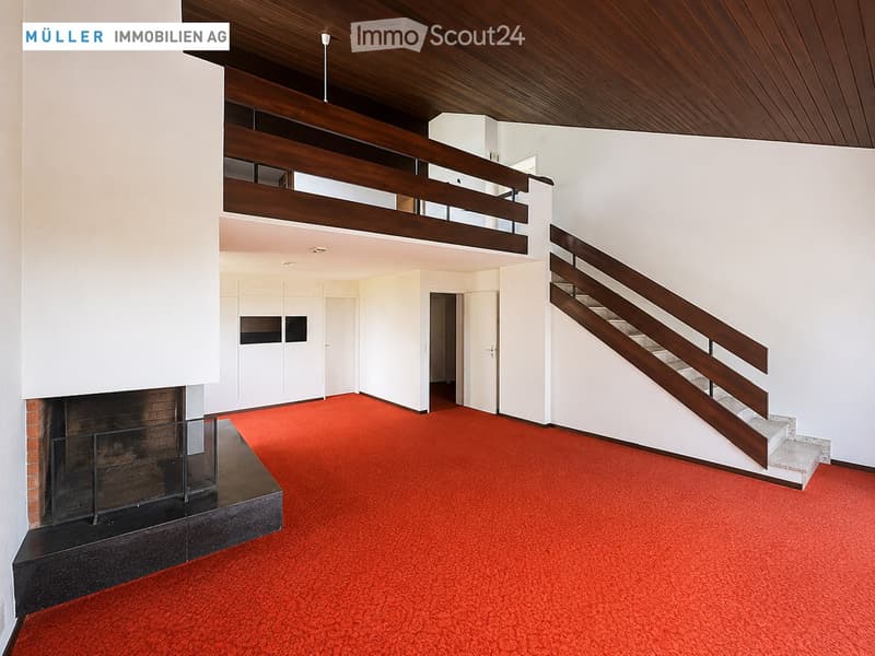Open hallway with red carpeting, white walls, wooden staircase, and fireplace.