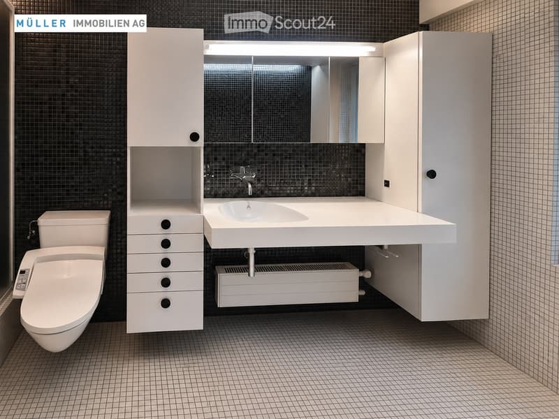 Modern bathroom with white tiles, a toilet, a sink with a large mirror, and built-in white cabinets.