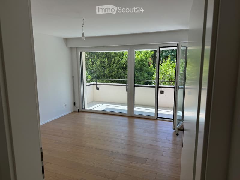 Empty room with wooden flooring, white walls, and large sliding glass doors leading to a balcony with a metal railing and outdoor space.