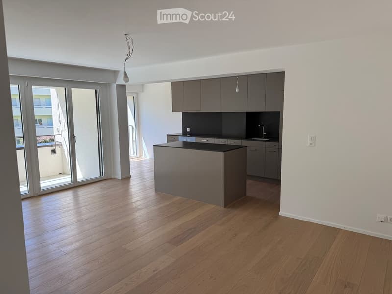 Modern kitchen with wooden flooring, grey cabinets, and a central island. Large sliding glass doors lead to a balcony.