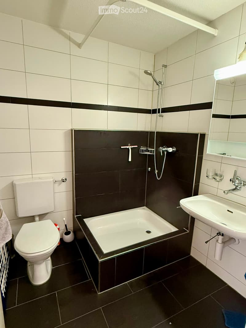 Modern bathroom with white tiles, black accents, a bathtub, toilet, sink, and showerhead.