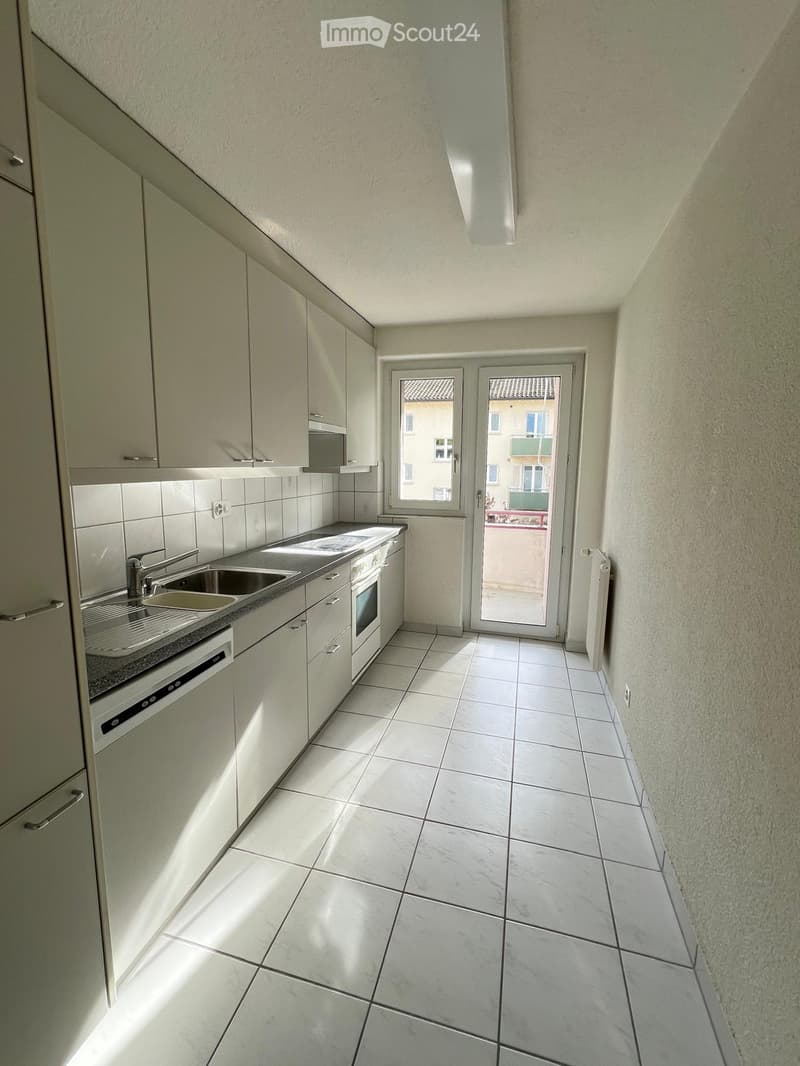 Modern kitchen with white tiled floor, white cabinets, stainless steel sink, oven, and dishwasher. Features a sliding glass door leading to a balcony.