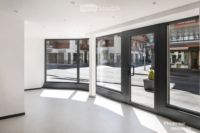 Empty room with large glass doors leading to a street view, white walls, and a grey floor.