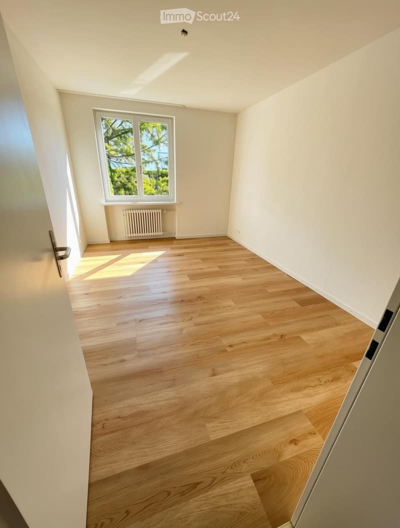 Empty room with light wooden flooring, white walls, and a large window with a view of trees. No furniture or equipment present.