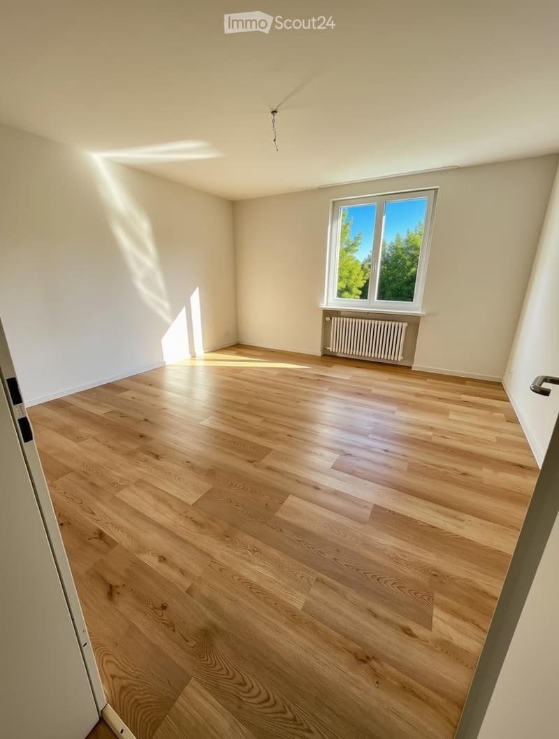 Empty room with light wooden flooring, white walls, and a large window letting in natural light. No furniture or equipment is present.