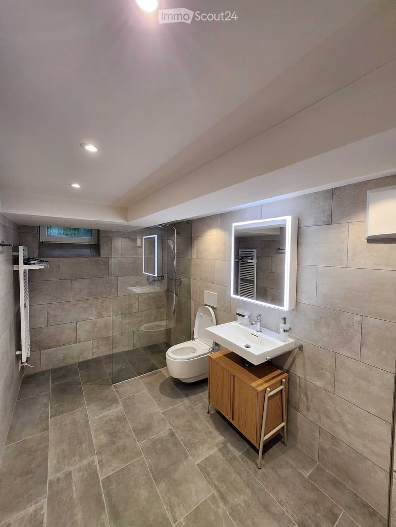 Modern bathroom with beige tiles, a white sink with a mirror, a toilet, and a glass-enclosed shower area.