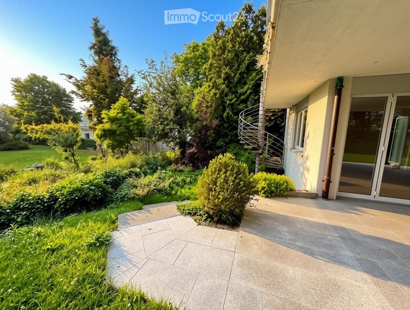 Well-maintained garden with a variety of trees, shrubs, and a paved patio area adjacent to a house with a spiral staircase leading to an upper level.