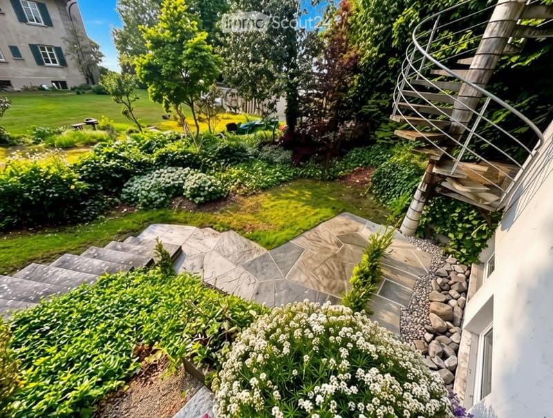 Well-maintained garden with a spiral staircase, stone pathways, lush greenery, and a bench in the background.