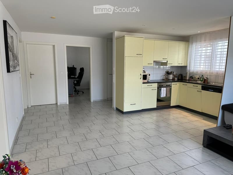 Bright kitchen with light-colored cabinets, tiled floor, and a small workspace area with a desk and chair.