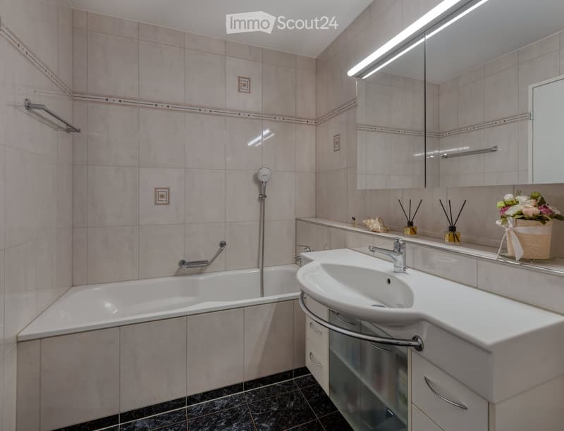 Modern bathroom with a bathtub, sink, large mirror, and decorative items on the counter.