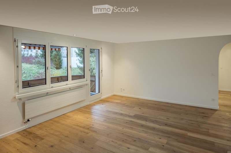 Empty room with light-colored wooden flooring, white walls, large windows with blinds, and a radiator below the windows.