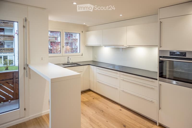 Modern kitchen with white cabinets, wooden flooring, and stainless steel appliances including an oven and sink.