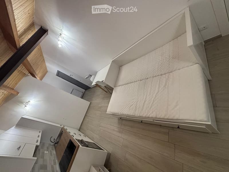 Modern bedroom with a large bed, a white chair, and built-in wardrobes. The room features wooden flooring and white walls.