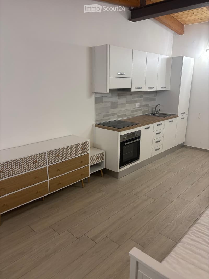 Modern kitchen with white cabinets, wooden countertops, and a built-in oven. Features a sink with a modern faucet and a small wooden side table with drawers.