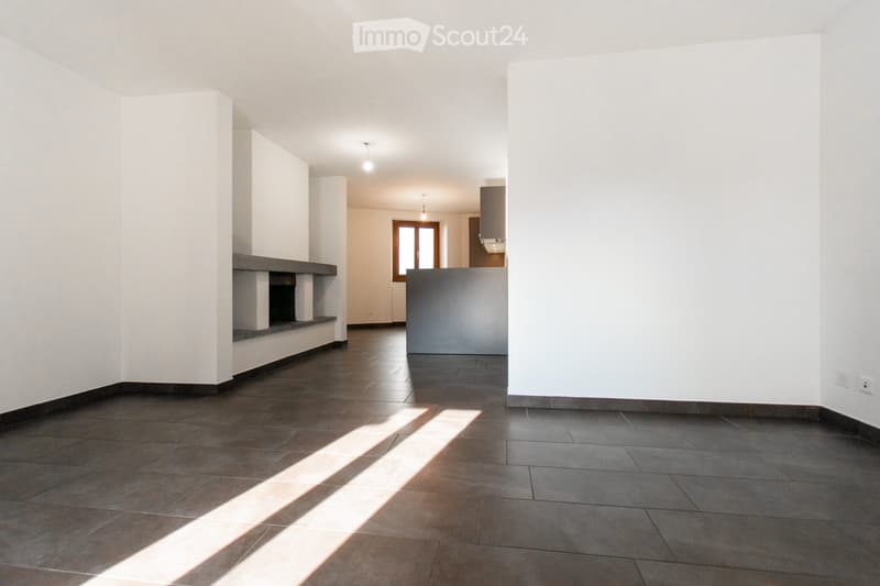 Empty room with dark tiled floor, white walls, and a built-in fireplace. Natural light streams in from a window in the background.