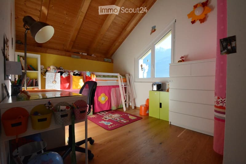 Bright, colorful children's bedroom with wooden floors, slanted wooden ceiling, bunk bed, desk, bookshelf, and colorful storage bins.