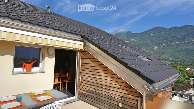 Balcony with outdoor dining setup, overlooking a mountain view. Includes a table with plates, cups, and chairs, along with an orange watering can on the windowsill.