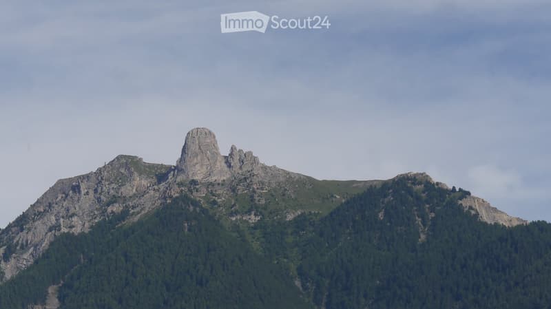 A mountain range with rocky peaks and dense forest cover, under a partly cloudy sky.