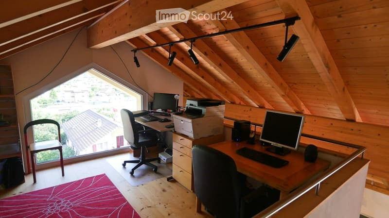 Cozy attic office with wooden beams, large skylight window, two desks with computers, chairs, printer, and storage cabinet.