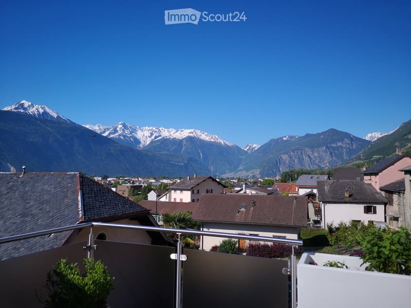 Balcony overlooking a town with houses and snow-capped mountains in the background.