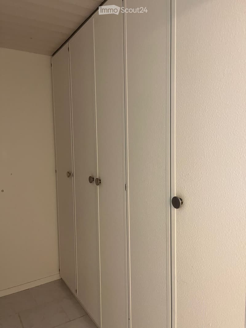 Empty hallway with beige walls, tiled floor, and closed doors with silver handles.