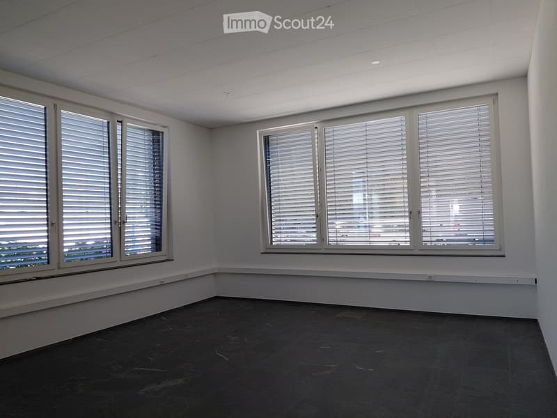 Empty room with white walls, dark tiled floor, and large windows with blinds.
