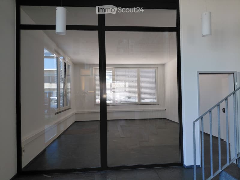 Empty hallway with glass doors, white walls, and a staircase on the right side.
