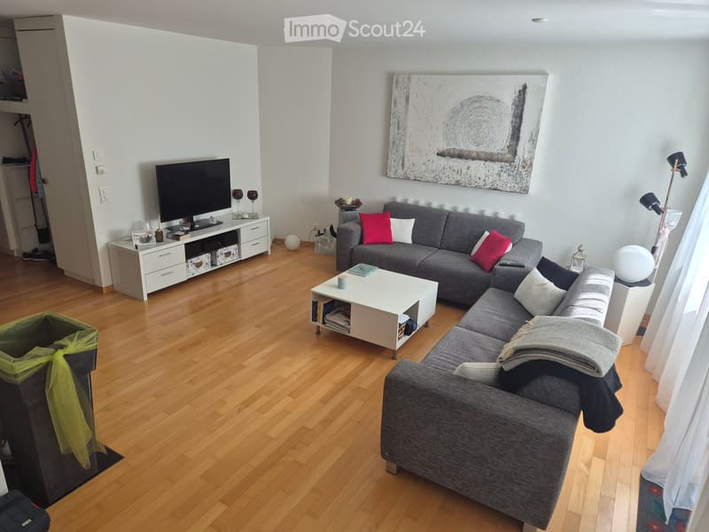Modern living room with wooden flooring, grey sectional sofa, white coffee table, TV stand, floor lamp, and decorative artwork on the wall.