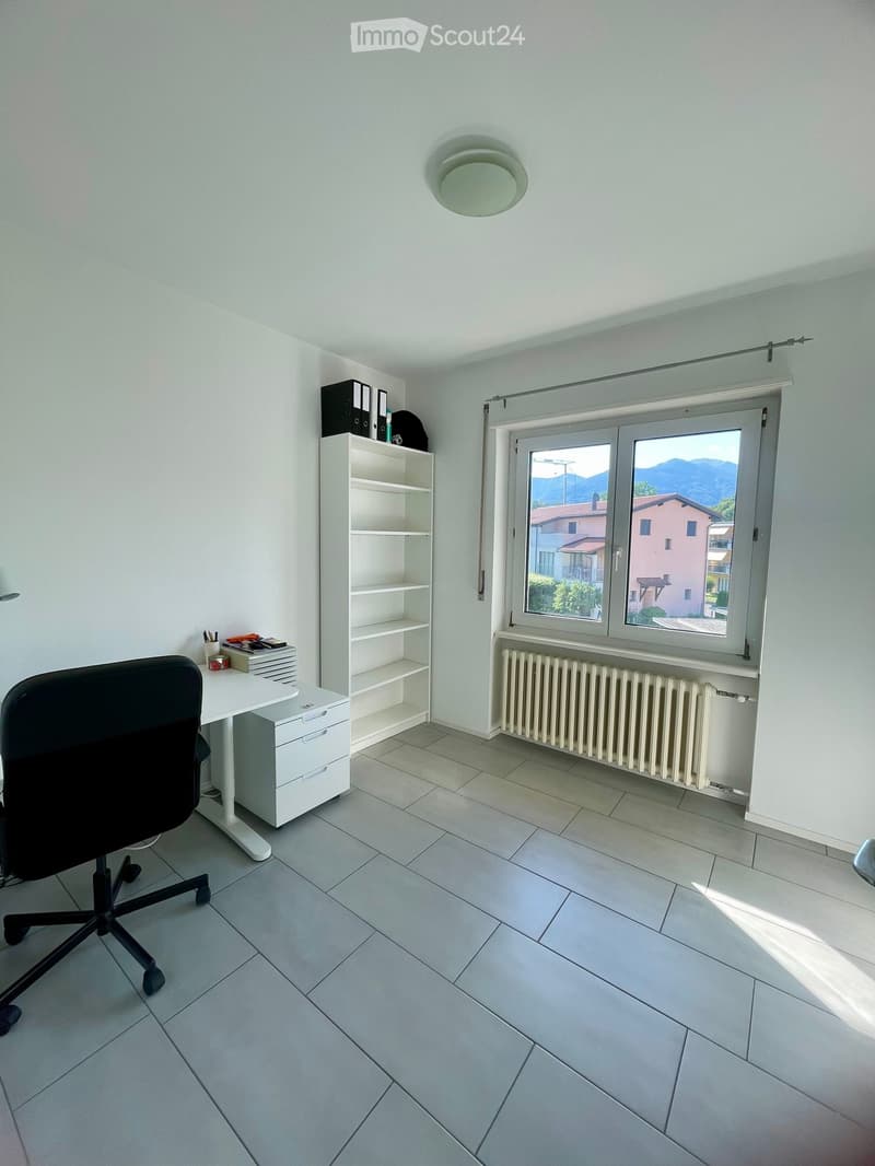 Office space with a white desk, black office chair, white shelving unit, radiator under a large window with a scenic view.