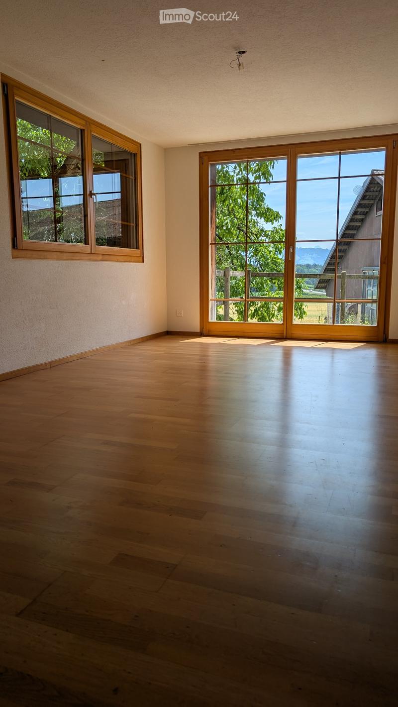 Empty room with wooden flooring, large windows, and sliding glass doors leading to an outdoor area.