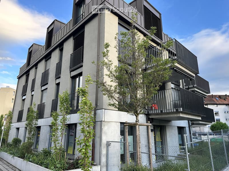 Building. Modern multi-story building with balconies, large windows, and contemporary design, surrounded by greenery and a fence.