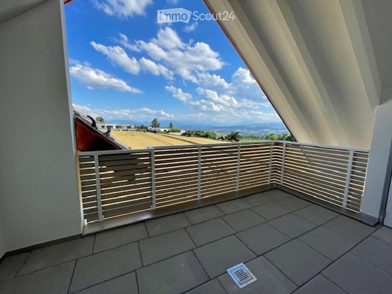 Balcony with tiled floor, white railing, and scenic view of fields and mountains under a partly cloudy sky.